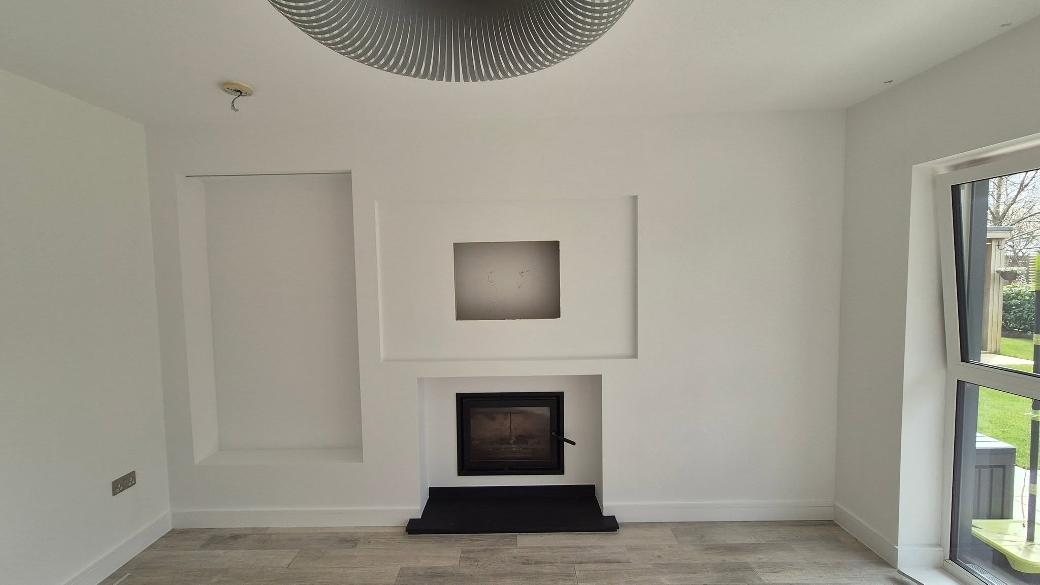 The finished wall in white with recessed niches around the wood burner