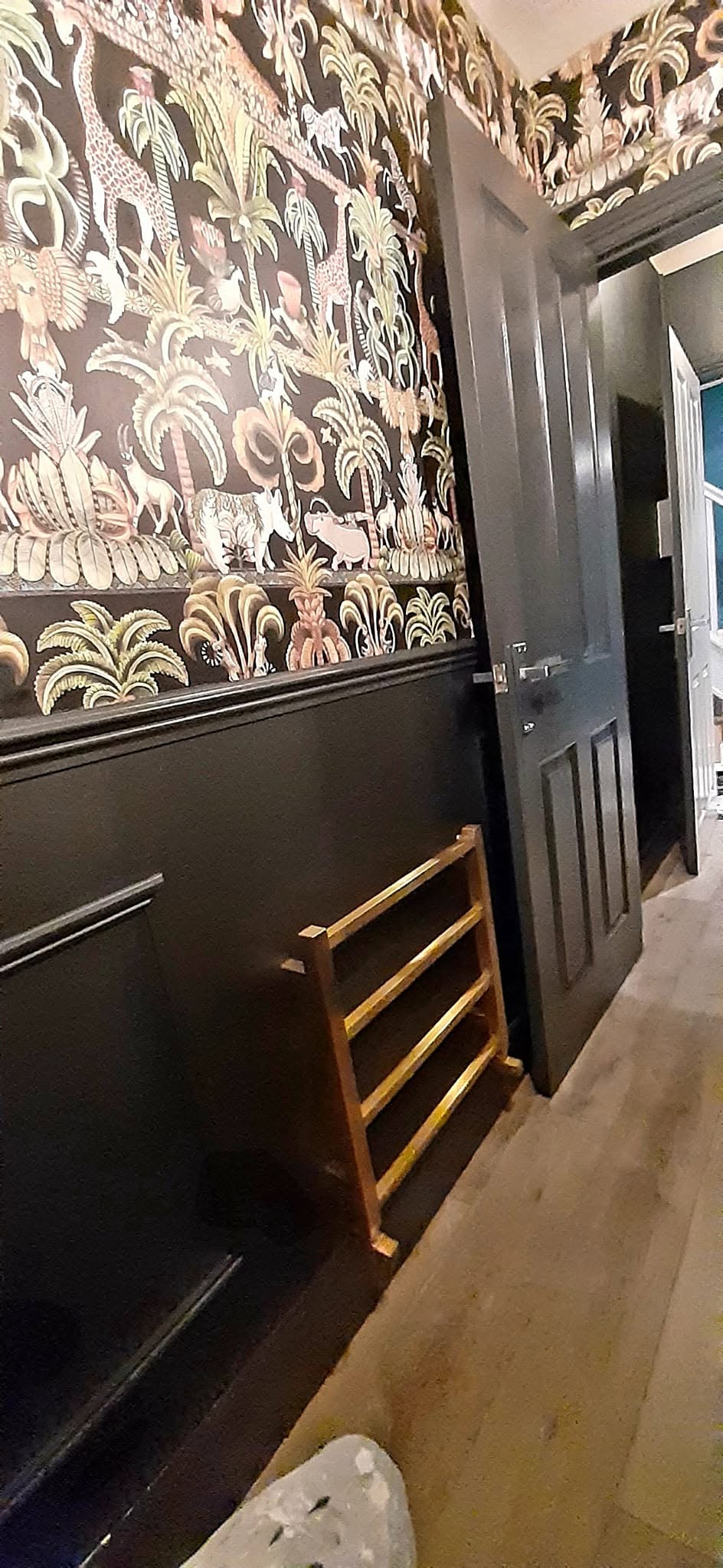 Cloakroom with dark panelling, patterned wallpaper and a dark painted door