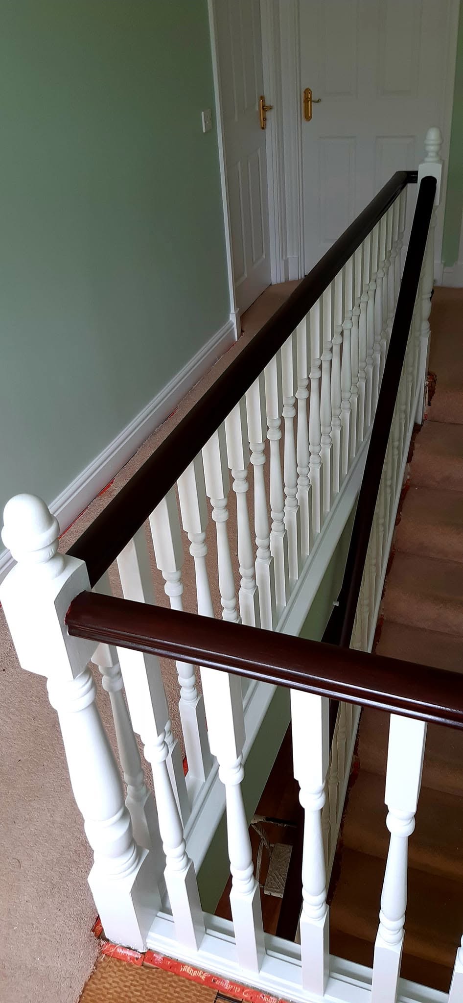 Staircase with a dark handrail, white spindles and sage green walls
