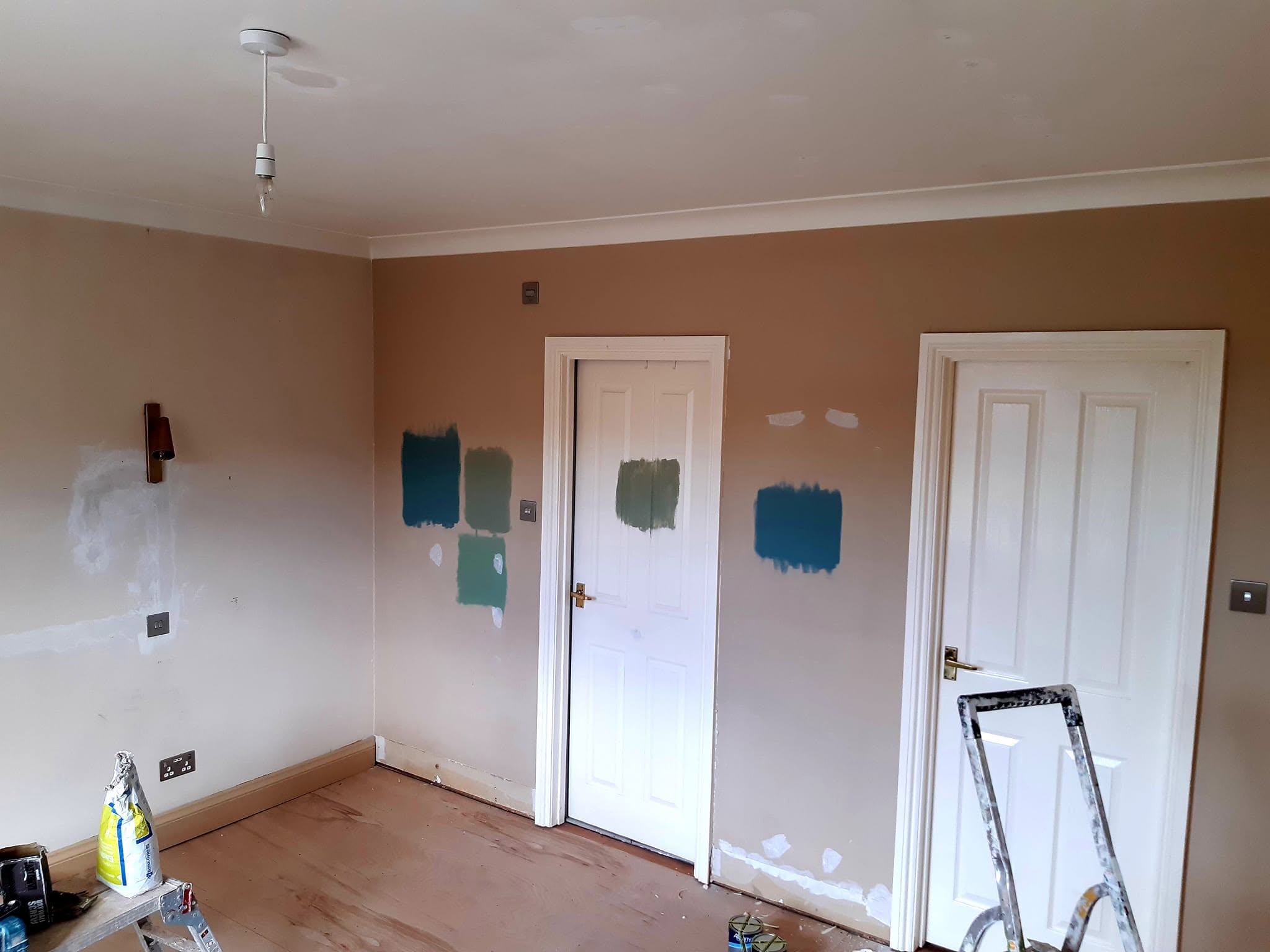 Bedroom walls on bare plaster with paint sample patches beside the doors