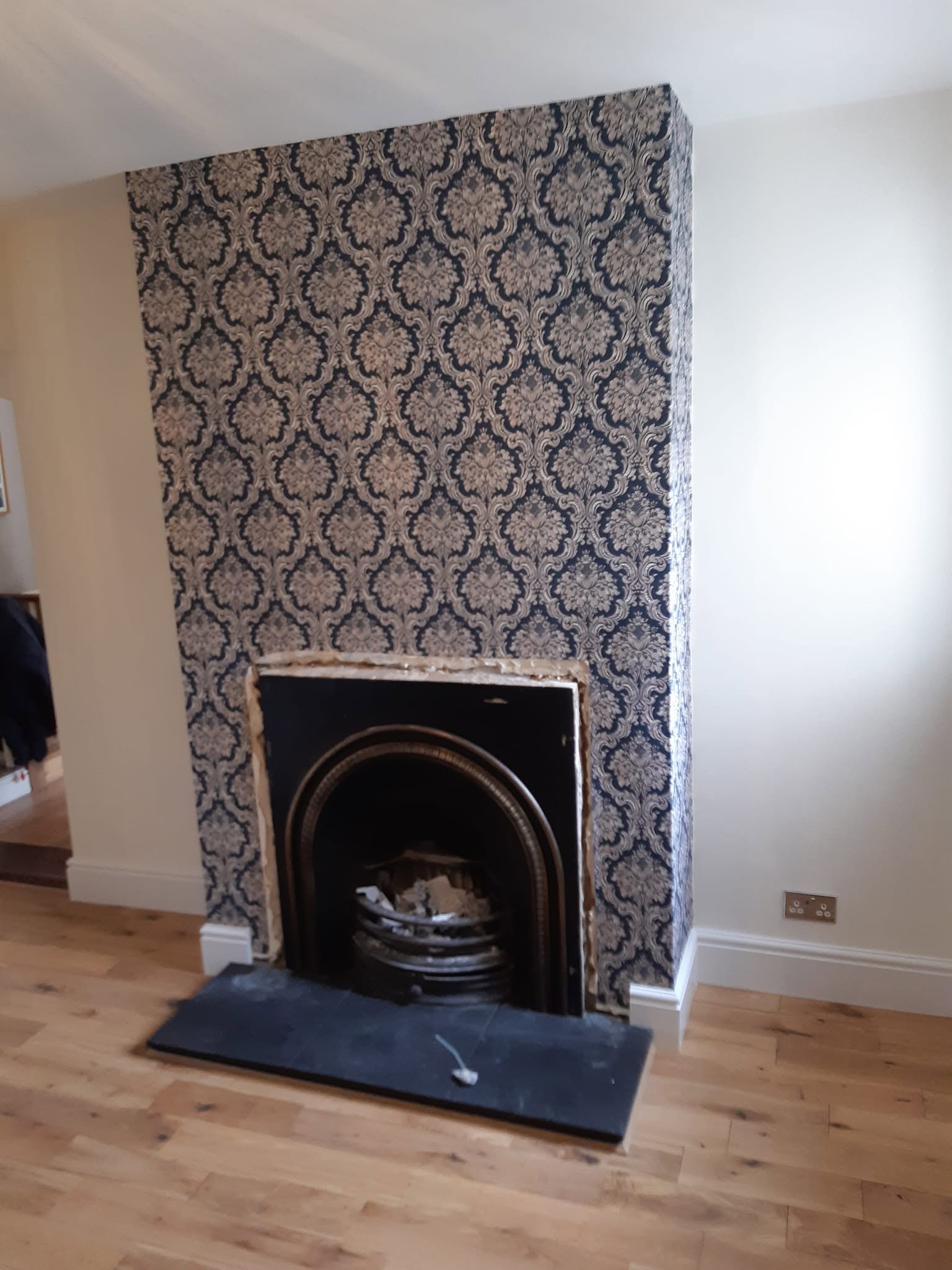 Chimney breast papered in damask around a cast iron fireplace